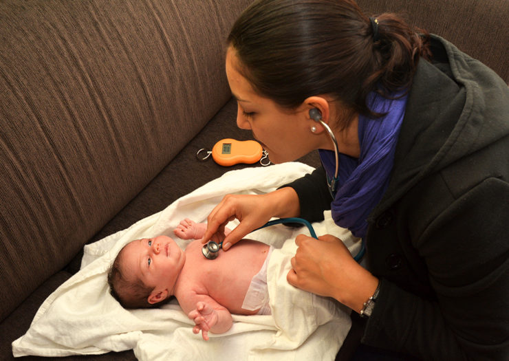 [Photo: A midwife checks the vitals of a newborn baby.]