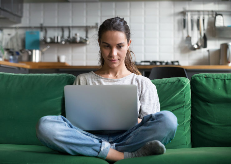 [Photo: Young woman at her computer, sitting on a couch.]
