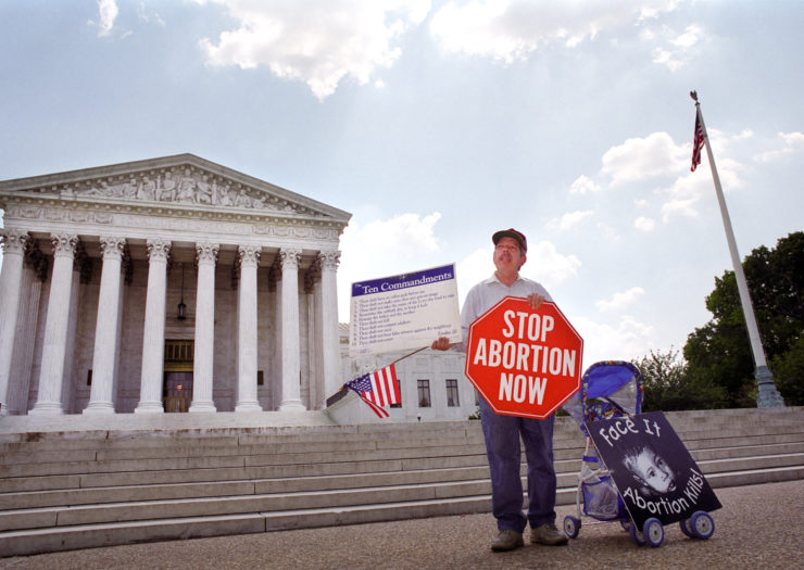 [Photo: A lone man stands in front of the U.S. Supreme Court with a sign that says 'Stop Abortion Now.']