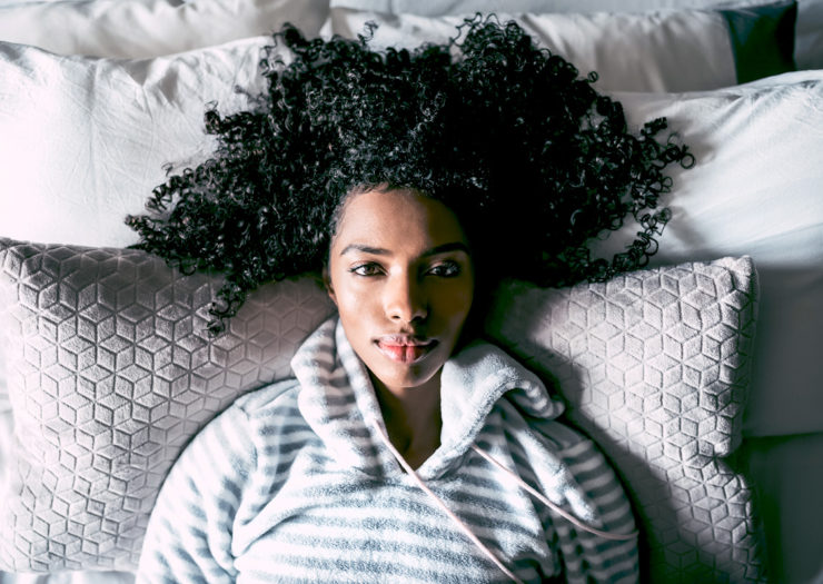 [Photo: A young Black woman lies on a bed looking up at the camera.]