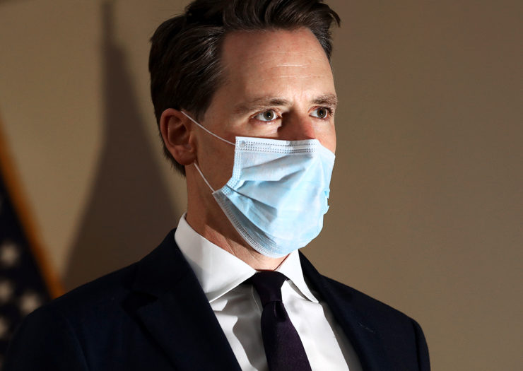 [Photo: Senator Josh Hawley wears a mask while he listens on during an event.]