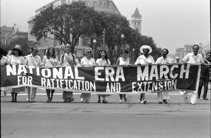 [Photo: Demonstrators carry a sign reading