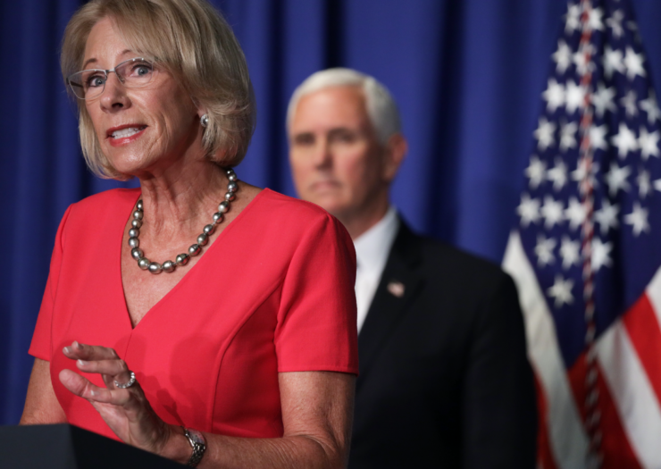 [Photo: Betsy DeVos speaking at the podium with Mike Pence behind her]