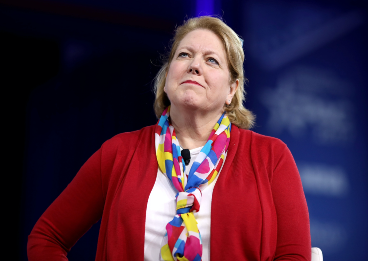 [PHOTO: Ginni Thomas stands in a red cardigan, white shirt, and colorful scarf]]