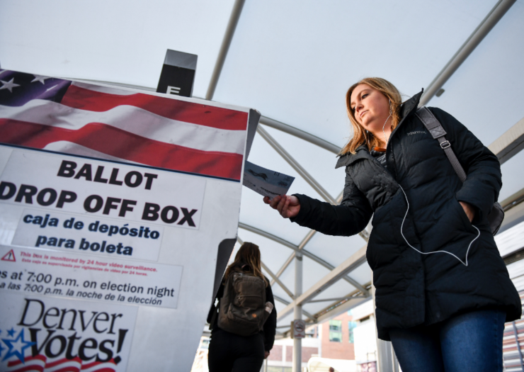 [PHOTO: A woman drops her ballot into a drop-off box]