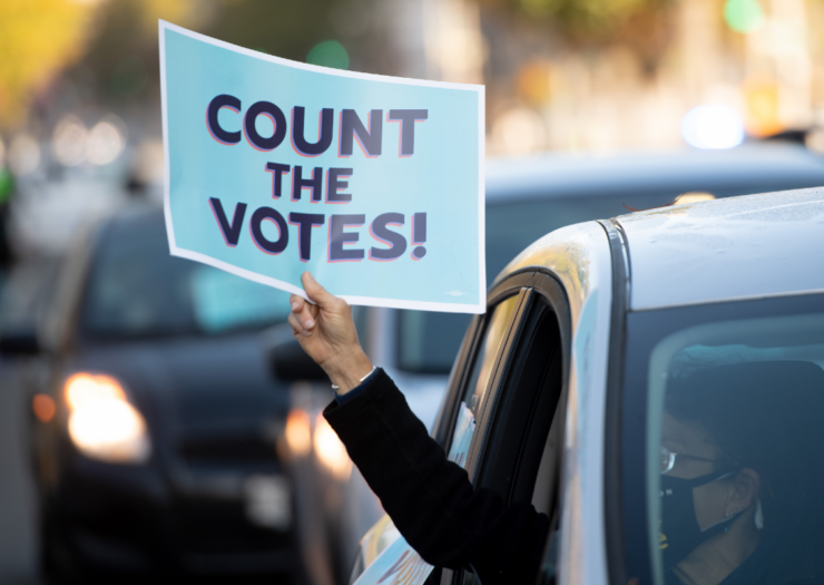 [PHOTO: A passenger in a car holds out a poster out the window that reads Count the Votes!]