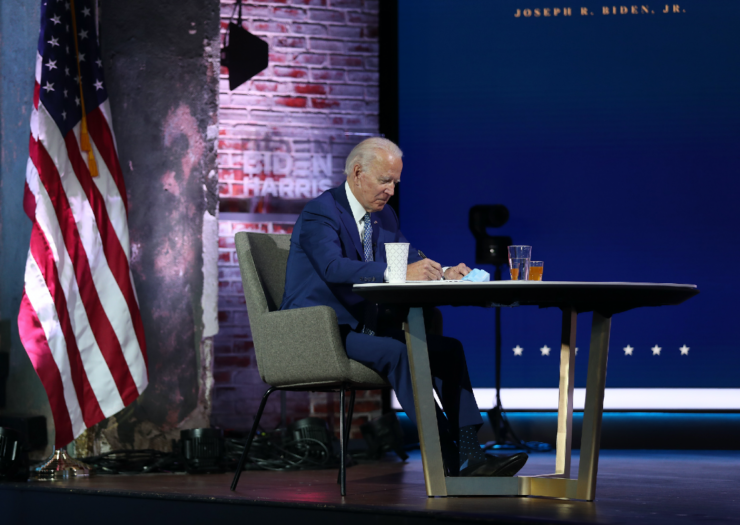 [PHOTO: Joe Biden sits behind a desk reading his briefing]