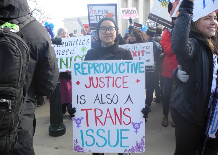 [Photo: A person holding a sign at a really that reads: Reproductive Justice Is Also A Trans Issue.]