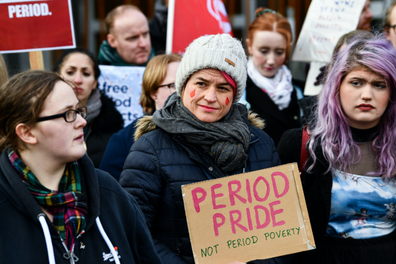 [PHOTO: Woman holding cardboard sign that reads
