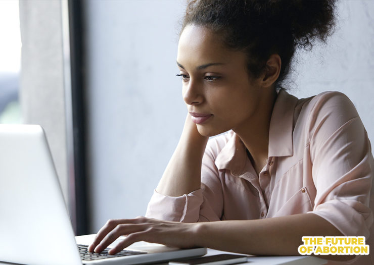 [Photo: A young Black woman sits in front of her open laptop.]