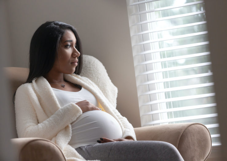 [PHOTO: Black pregnant woman with hands on belly looks pensive]