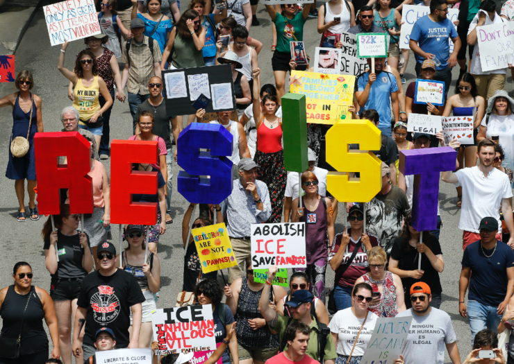 [PHOTO: Crowd of people gathered at a protest, holding letters that spell out RESIST]