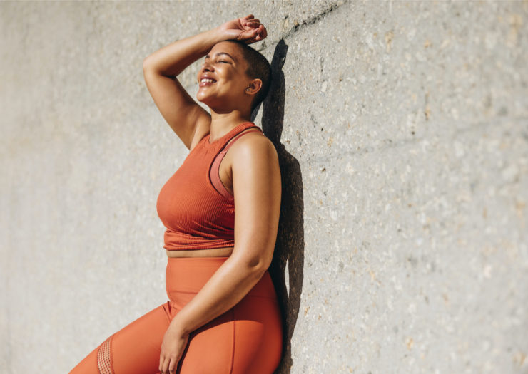 [PHOTO: Woman wearing orange workout clothes smiling in the sun]