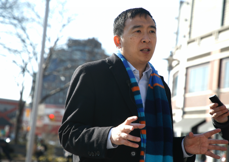 [PHOTO: Andrew Yang holding hands out while talking to media]