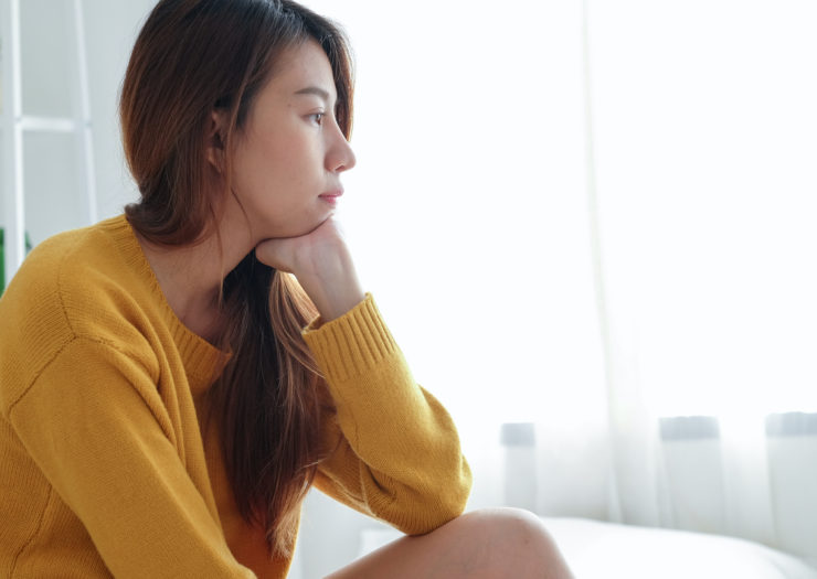 [PHOTO: Asian woman with long hair and wearing yellow short looks pensive]