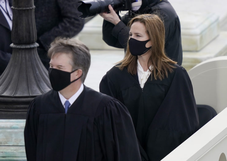 Brett Kavanaugh and Amy Coney Barrett both facing left wearing Supreme Court robes and black masks