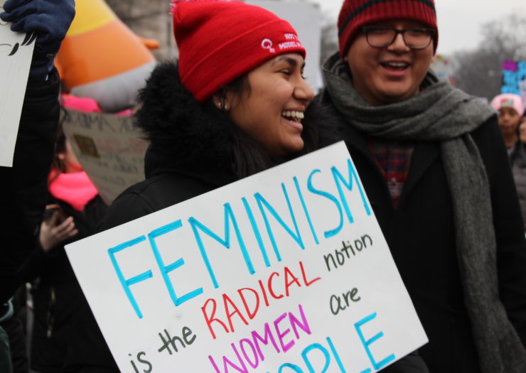 Photo of protester holding sign that reads feminism is the radical notion that women are people