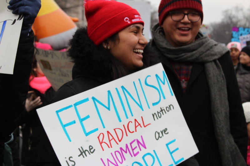 Photo of protester holding sign that reads feminism is the radical notion that women are people