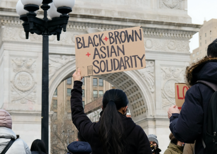 Photo of the back of a woman holding a sign that reads Black brown Asian solidarity