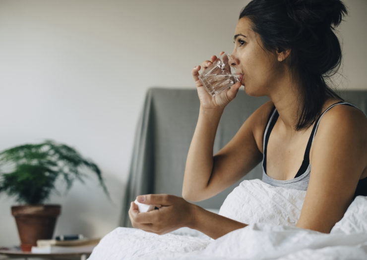 Photo of woman in bed drinking water with pills