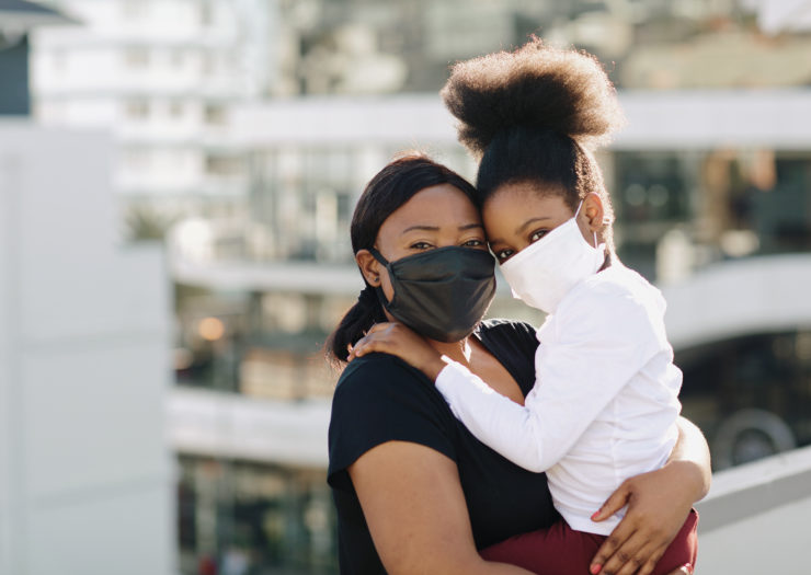 Photo of Black woman holding her child and both are wearing masks