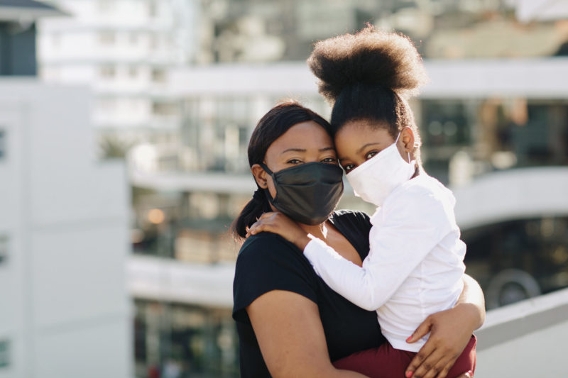 Photo of Black woman holding her child and both are wearing masks