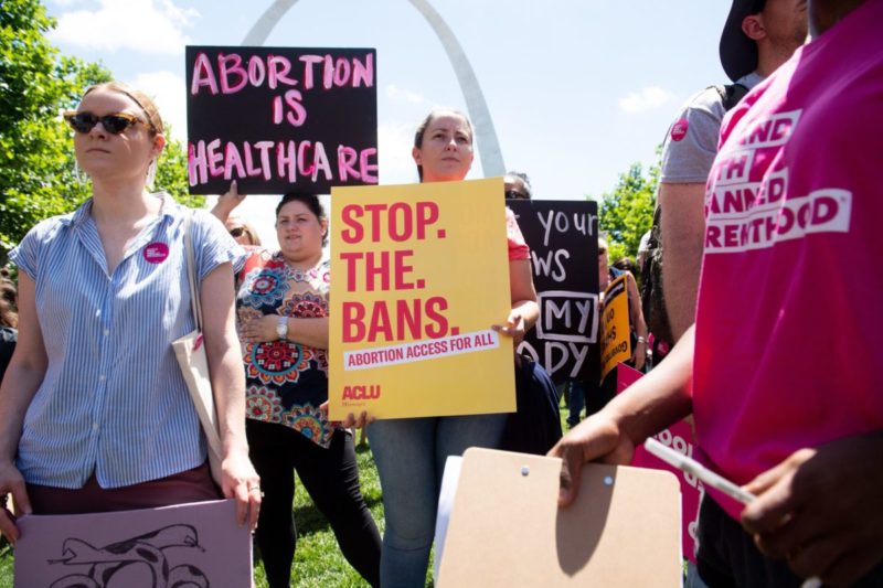 Photo of protesters with a sign that reads stop the bans and another sign that says abortion is health care