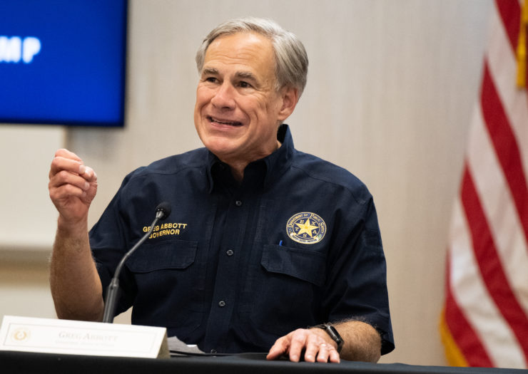 [Governor Greg Abbott speaks at a podium while dressed in a navy shirt with a badge that says Texas public safety]