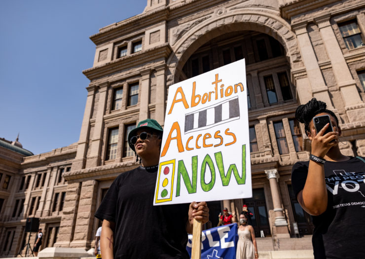 A protester in front of the Texas Capitol building carrying a sign that reads Abortion Access Now