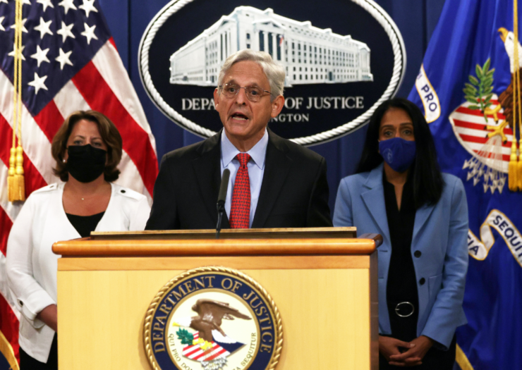 Attorney General Merrick Garland speaks behind a podium as Deputy Attorney General Lisa Monaco is on the left and Associate Attorney General Vanita Gupta is on the right