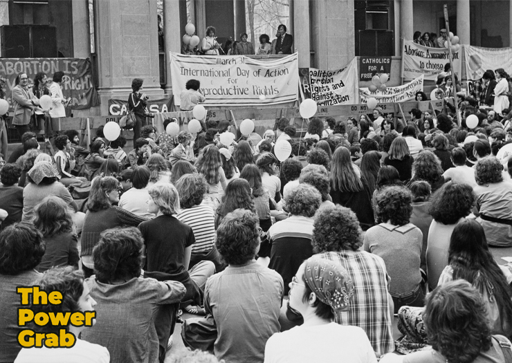 Black and white photo of a large crowd sitting and facing a sign that reads International Day of Abortion