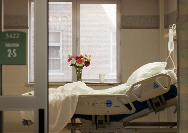 Photo of vacant hospital bed in room with flowers and IV bag