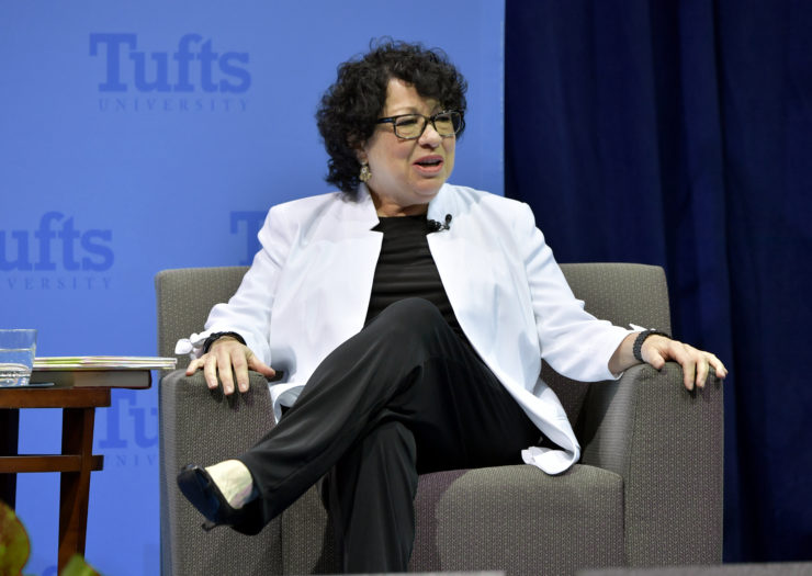 Photo of Justice Sonia Sotomayor sitting cross-legged in an armchair while speaking onstage