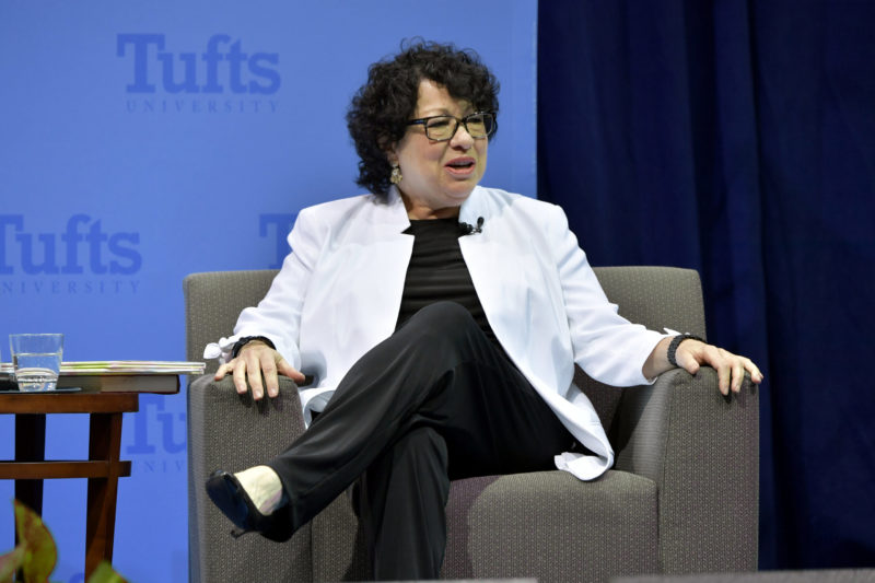 Photo of Justice Sonia Sotomayor sitting cross-legged in an armchair while speaking onstage