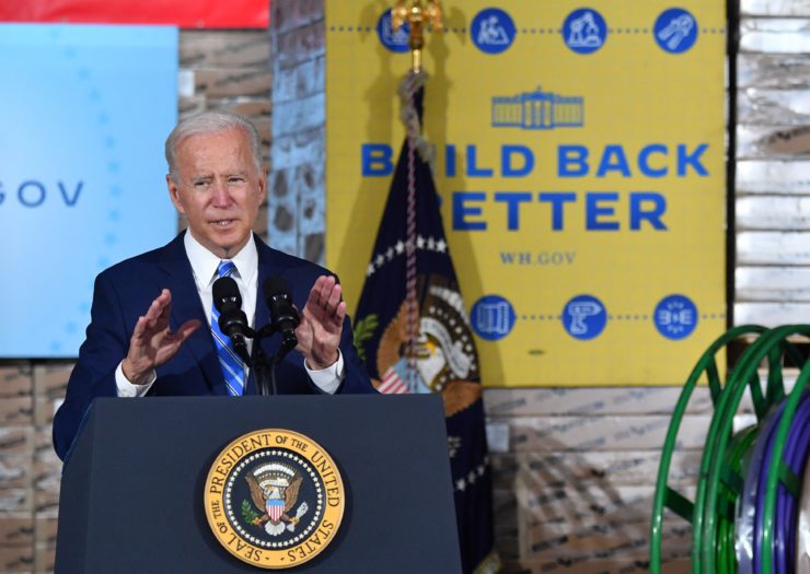 Photo of Joe Biden speaking behind podium with yellow and blue sign that says build back better