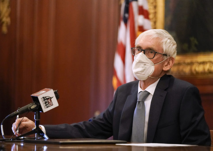 Photo of Wisconsin governor Tony Evers wearing a mask and sitting behind a desk with a microphone