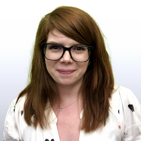 Headshot image of Becca Andrews, a white woman with medium length red hair and glasses