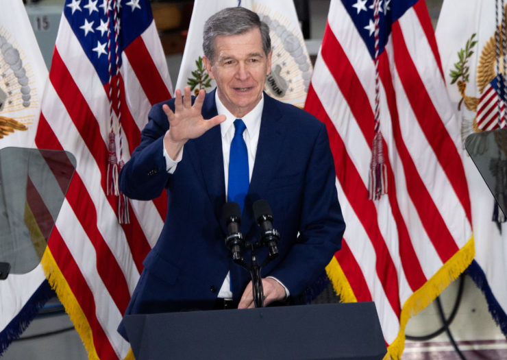 Photo of North Carolina Governor Roy Cooper standing in front of American flags and behind a podium speaking