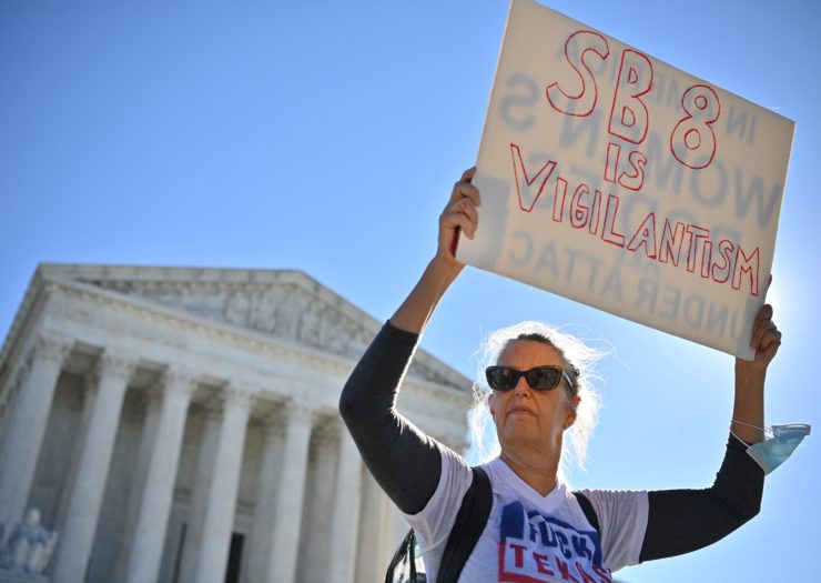 Photo of abortion activist in front of the Supreme Court holding a white sign with red lettering that says SB 8 is vigilantism