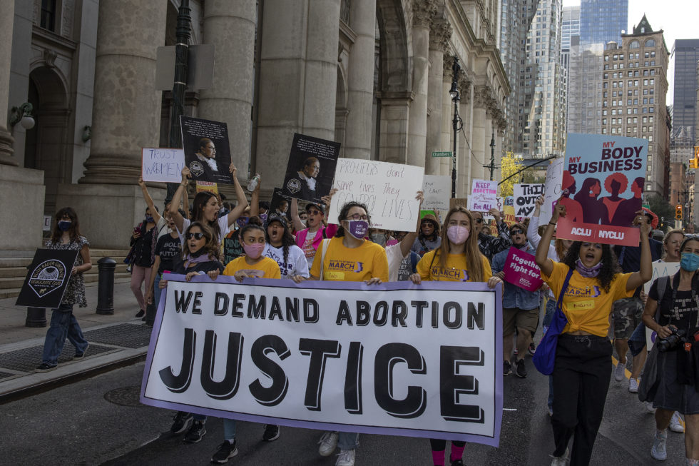 Photo of group of protesters carrying a banner that reads we demand abortion justice