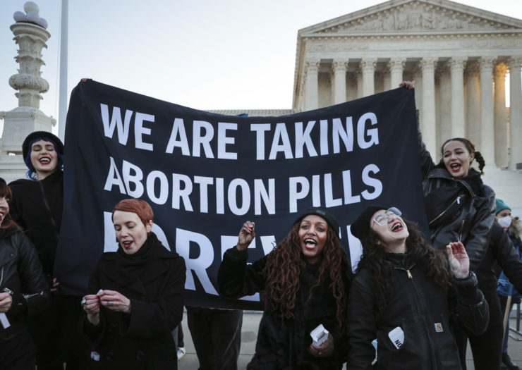 Photo of abortion rights activist holding a giant banner that reads we are taking abortion pills forever and standing outside the Supreme Court building