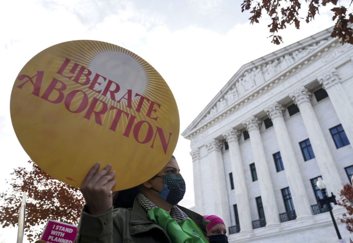 Photo of abortion rights protester in front the Supreme Court holding a round yellow sign that reads Liberate Abortion