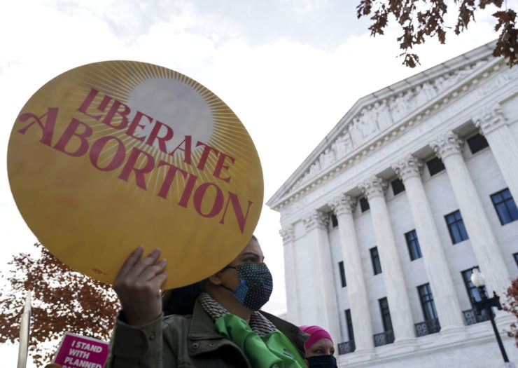 Photo of abortion rights protester in front the Supreme Court holding a round yellow sign that reads Liberate Abortion