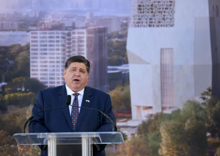 J.B. Pritzker stands at podium in front of Obama Presidential Center.