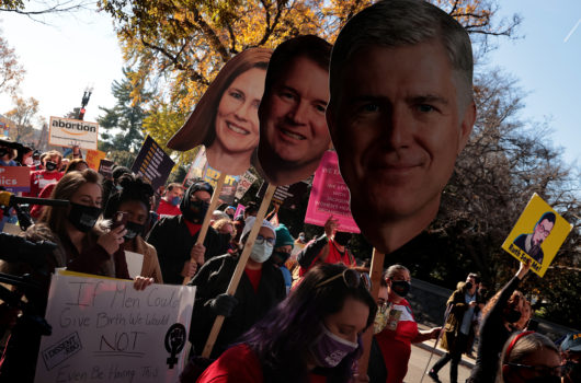 Abortion activists holding photos of Supreme Court justices heads on a stick.