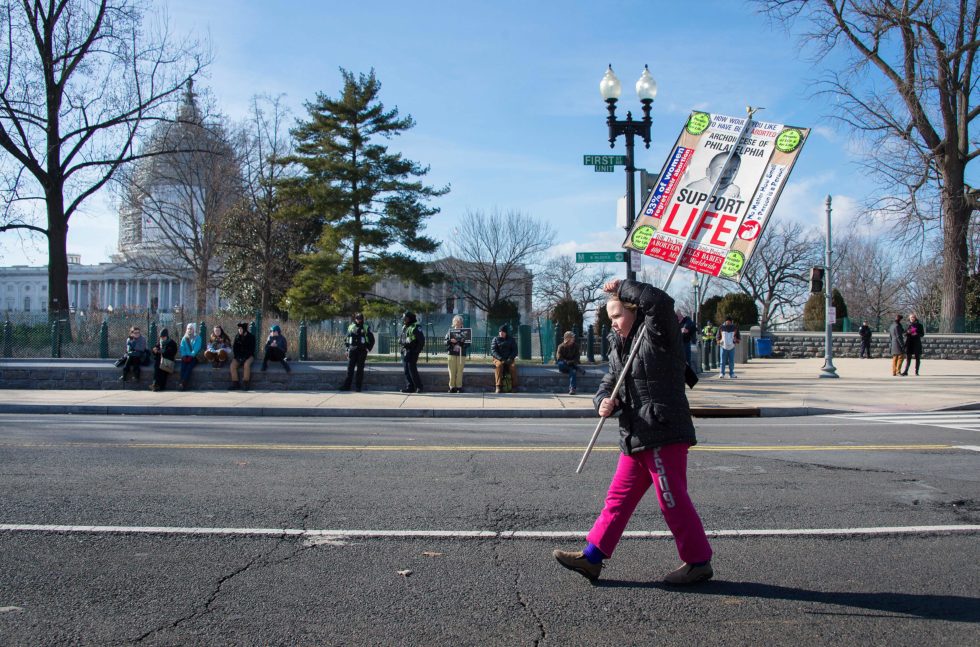 Photo of a young girl marching down an empty street with a sign