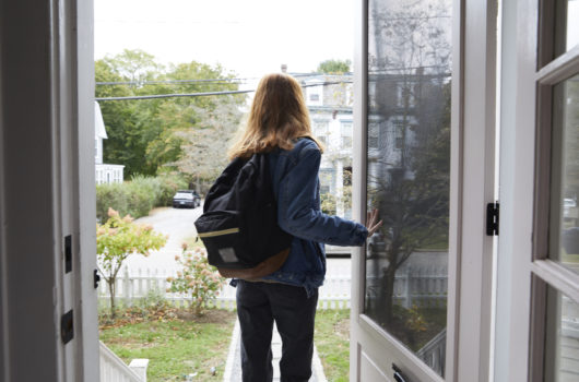 Photo of teen with backpack holding door while walking out
