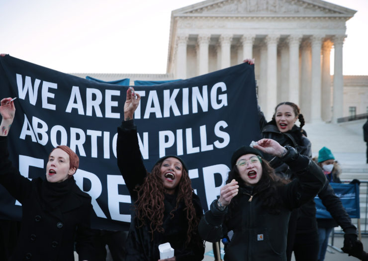 Photo of activists standing in front of a large banner that reads we are taking abortion pills forever