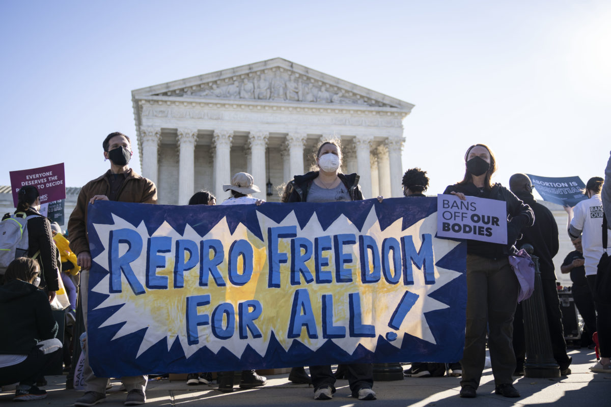 Photo of pro-choice activists holding a large sign that reads repro freedom for all outside the U.S. Supreme Court