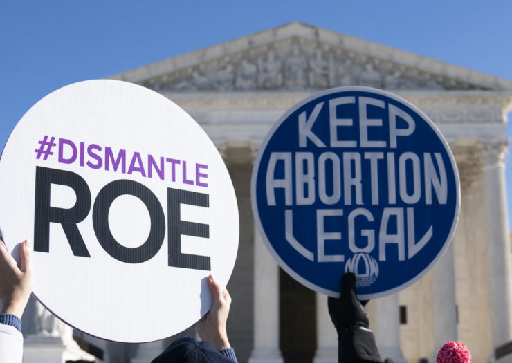 Photo of two signs in front of the Supreme Court - one says #Dismantle Roe and the other Keep Abortion Legal